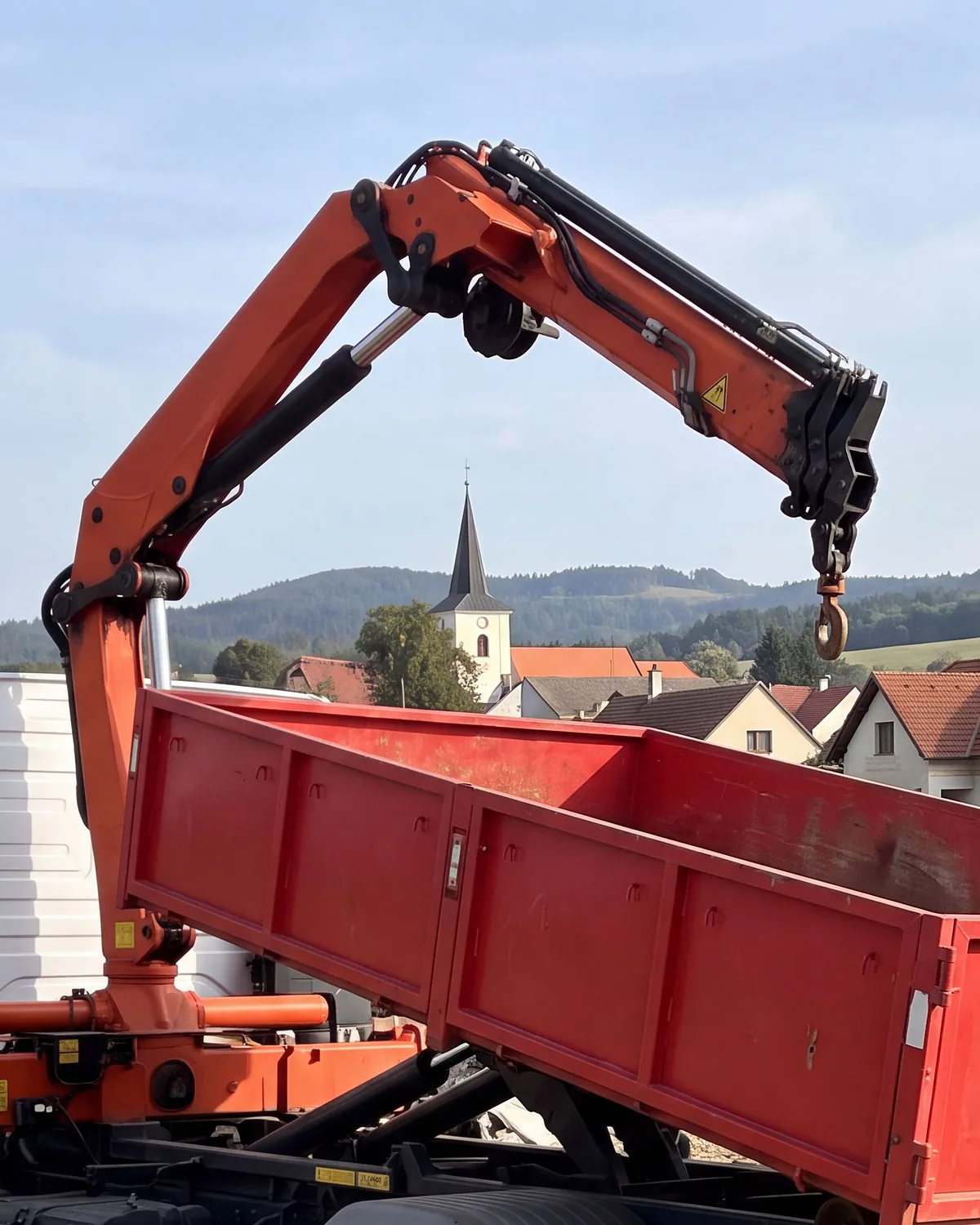 Vysunutá hydraulická ruka s hákem nad střechami obce