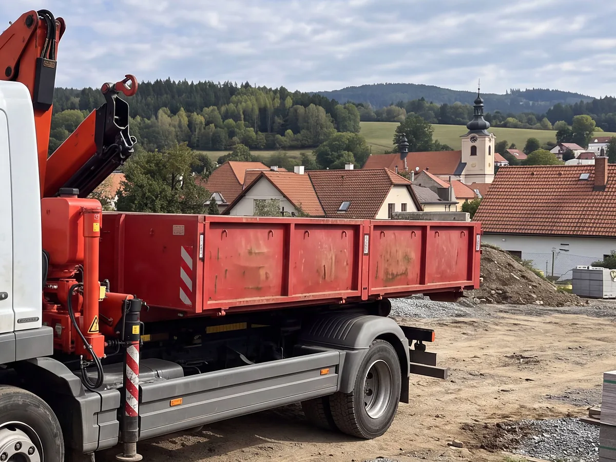 Kontejner na nosiči před obcí s kostelem a zalesněnými kopci