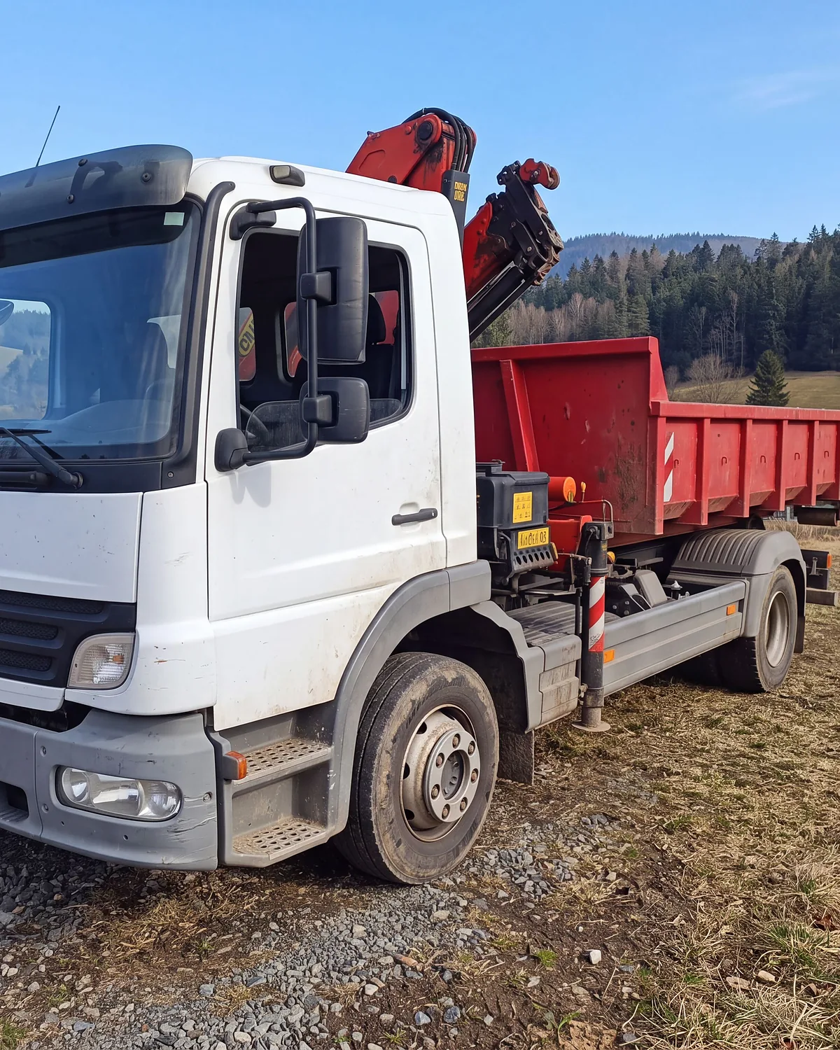 Nákladní vůz Mercedes-Benz Atego s hákovým nosičem a složenou hydraulickou rukou u obce